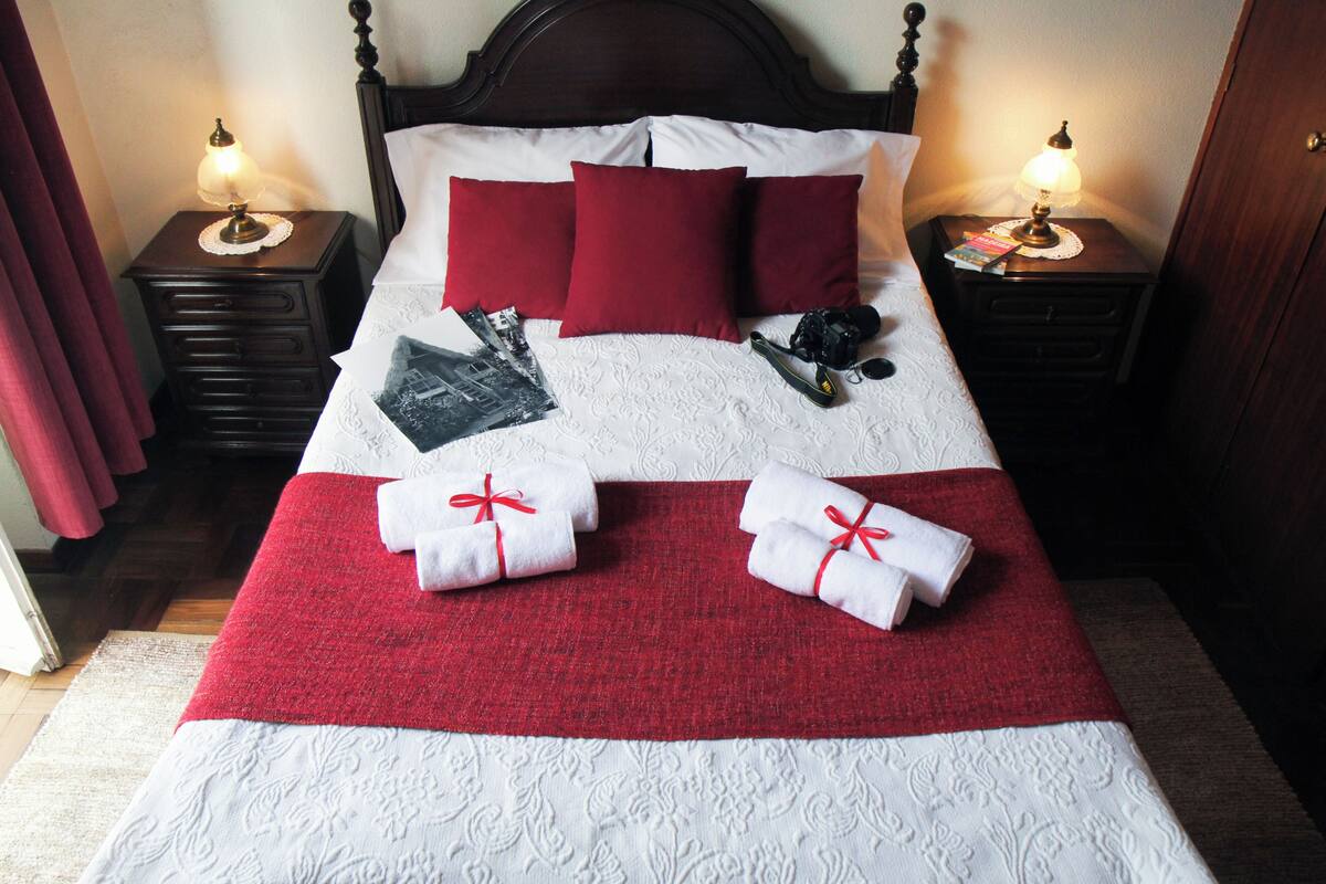 Un lit bien fait, avec une literie rouge et blanche, deux tables de chevet avec des lampes et un plaid rouge.