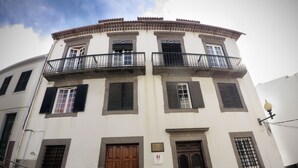 Un immeuble à plusieurs étages, doté d’une façade blanche, de balcons et d’un mélange de portes en bois et en métal.