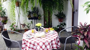 Une terrasse couverte avec une nappe à carreaux, deux chaises et diverses plantes en pot.