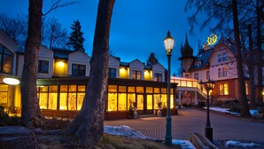 A building with large windows and a balcony, surrounded by trees and a snow-covered ground. - Hotel Szrenicowy Dwór (Szklarska Poreba)
