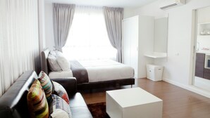 A modern hotel room with a bed, a sofa, a coffee table, and a small kitchen area. - Baan Khun Koey A414 by Huahin Holiday Condo (Hua Hin)