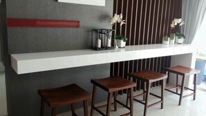 A modern bar area with a white countertop, wooden stools, and decorative plants. - Baan Khun Koey A414 by Huahin Holiday Condo (Hua Hin)