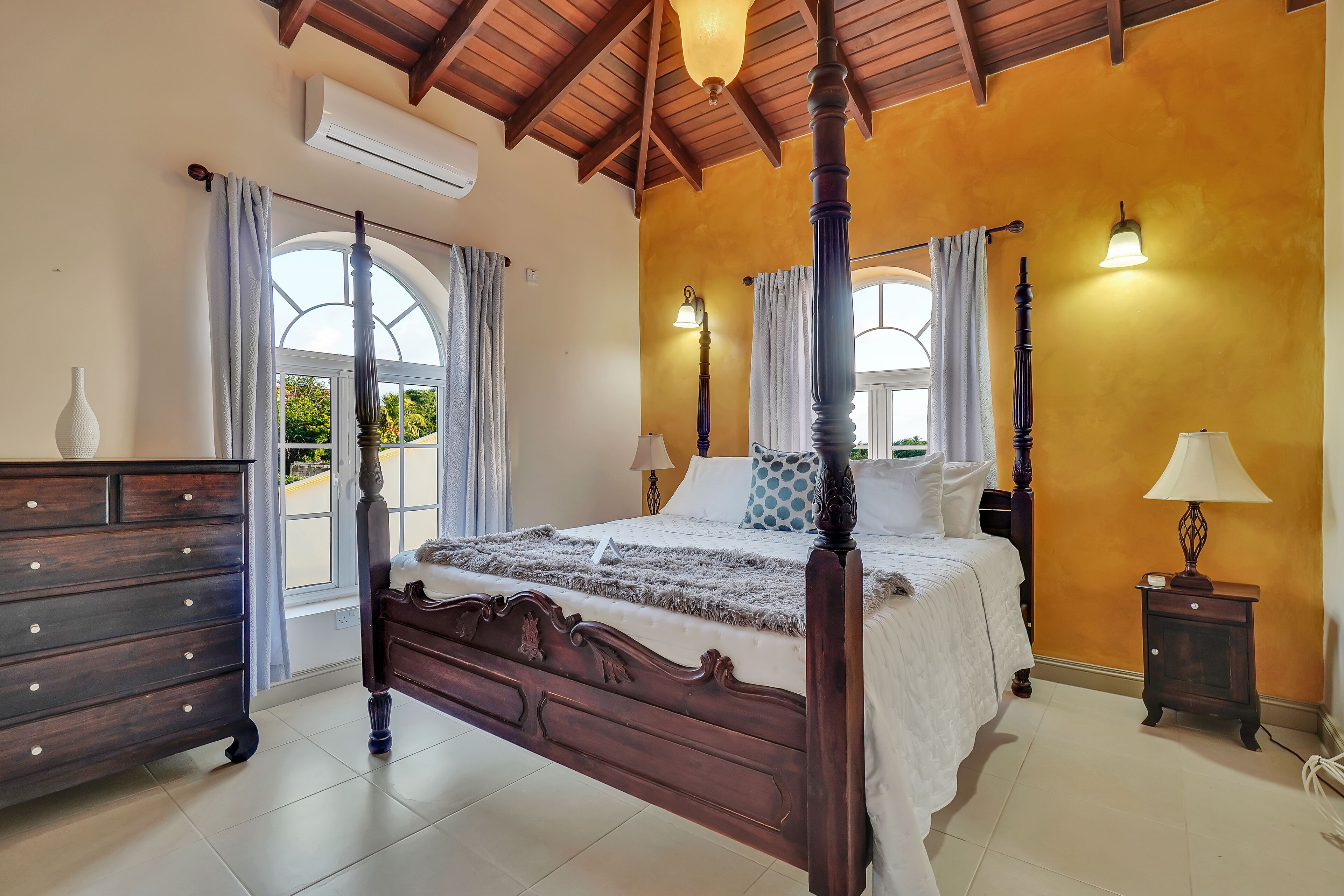 Un dormitorio con cama con dosel, cómoda de madera, mesita de noche y lámpara.