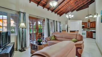 A spacious living room with a large sofa, a television, and a dining area in the background.