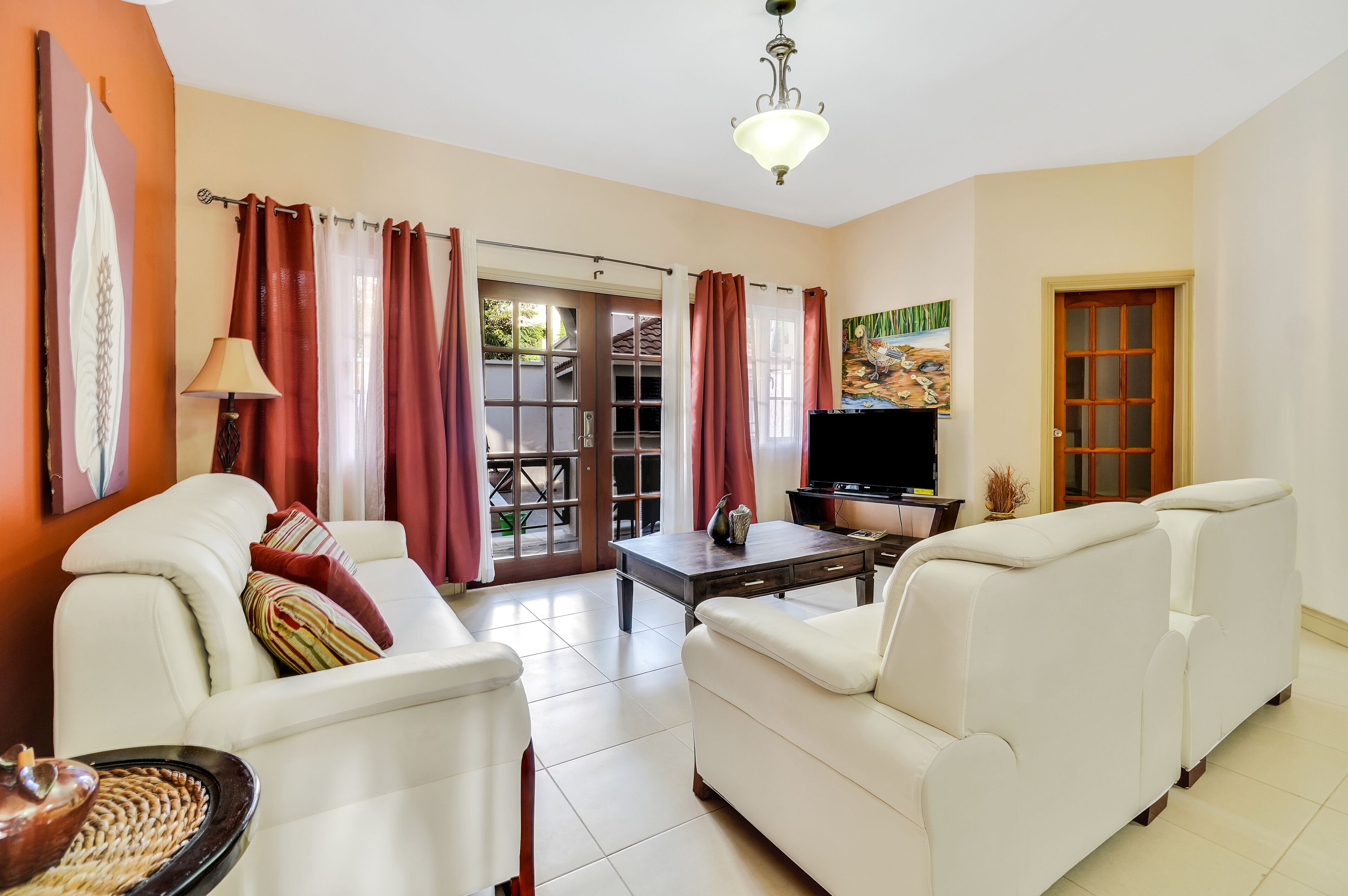 A living room with a sofa, a TV, a table, and a door leading to a balcony.