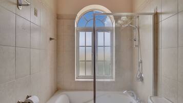 Un baño con ducha envuelta en vidrio, bañera y ventana con vistas.