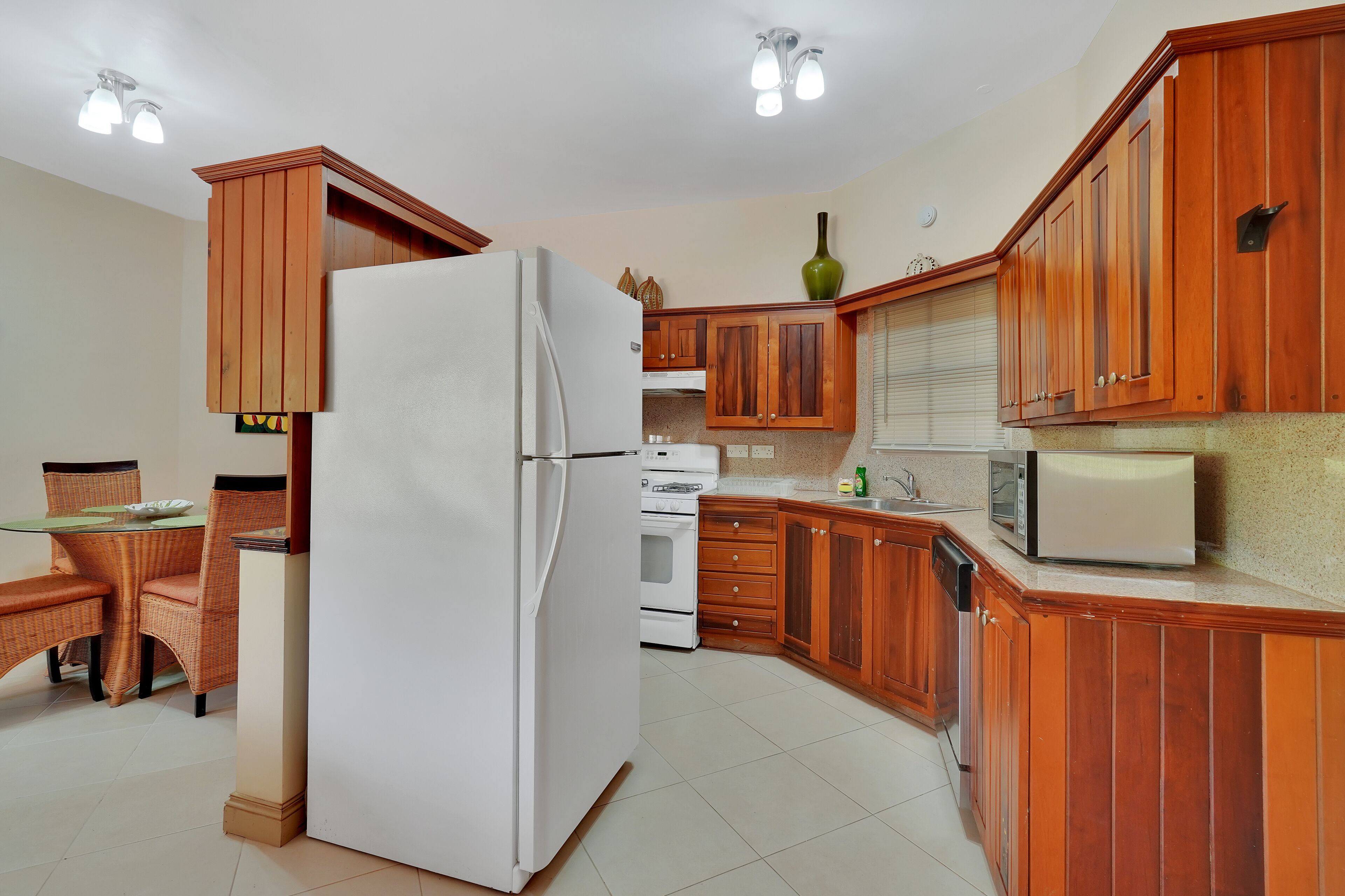 Una cocina con armarios de madera, un refrigerador, un microondas y un comedor con mesa y sillas.