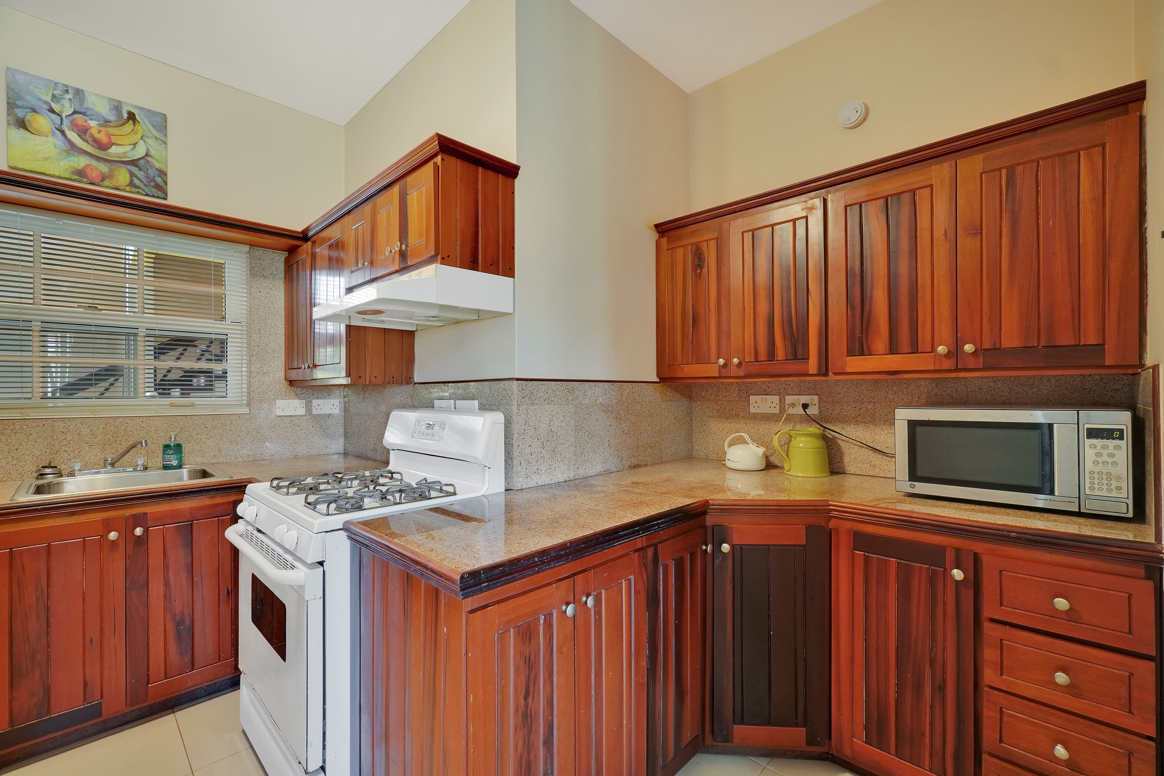 Une cuisine avec des meubles de rangement en bois, une cuisinière, un four à micro-ondes et une fenêtre  équipée de stores.