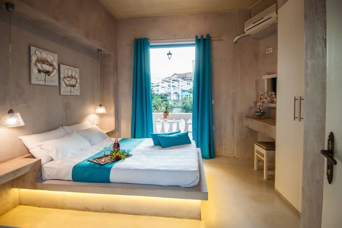 Une chambre à coucher avec un lit, une table de chevet, une fenêtre avec des rideaux, une petite table et une chaise.