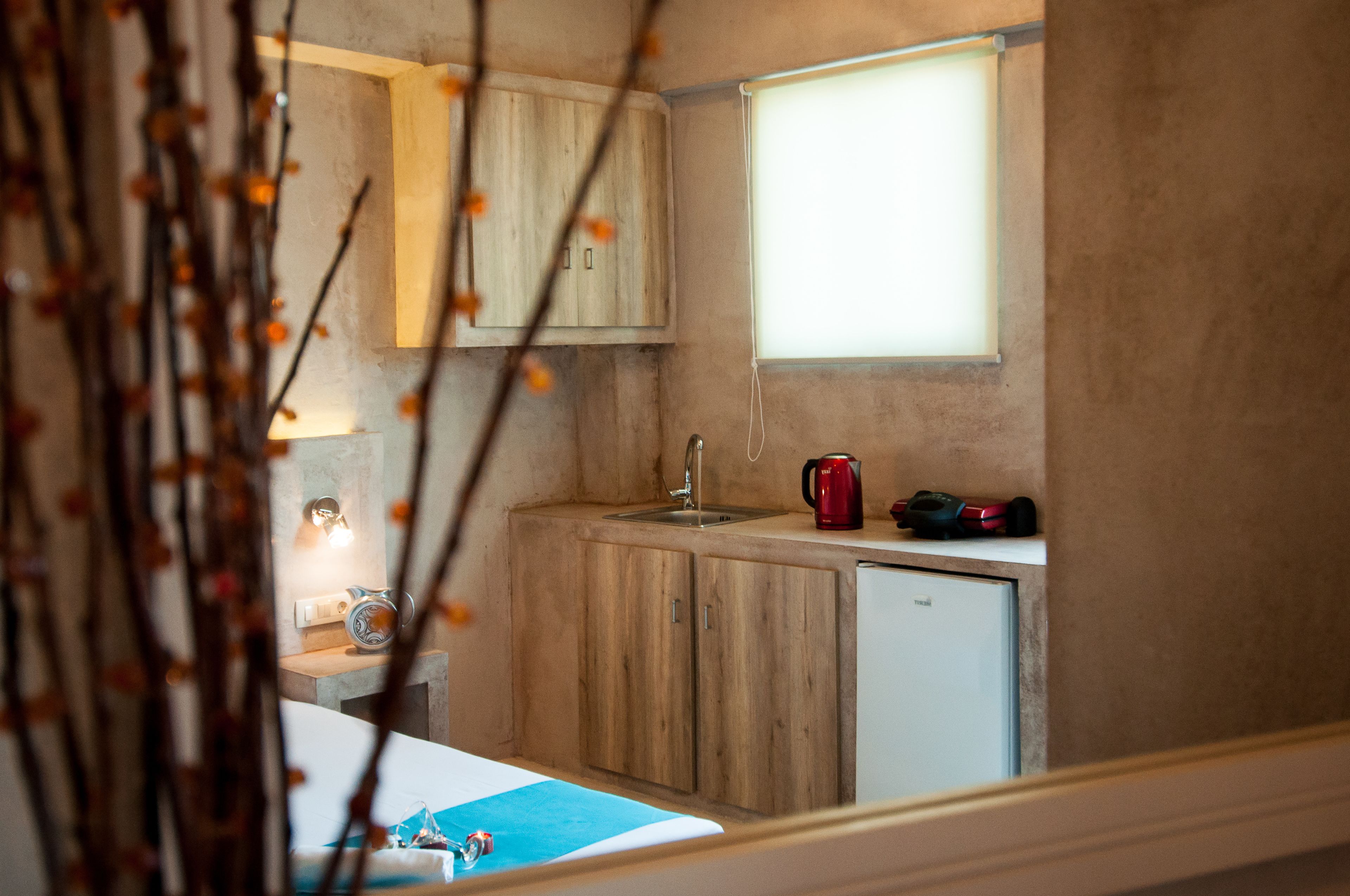 Cocina compacta con gabinetes de madera, un lavamanos, un refrigerador pequeño y una ventana con persianas.