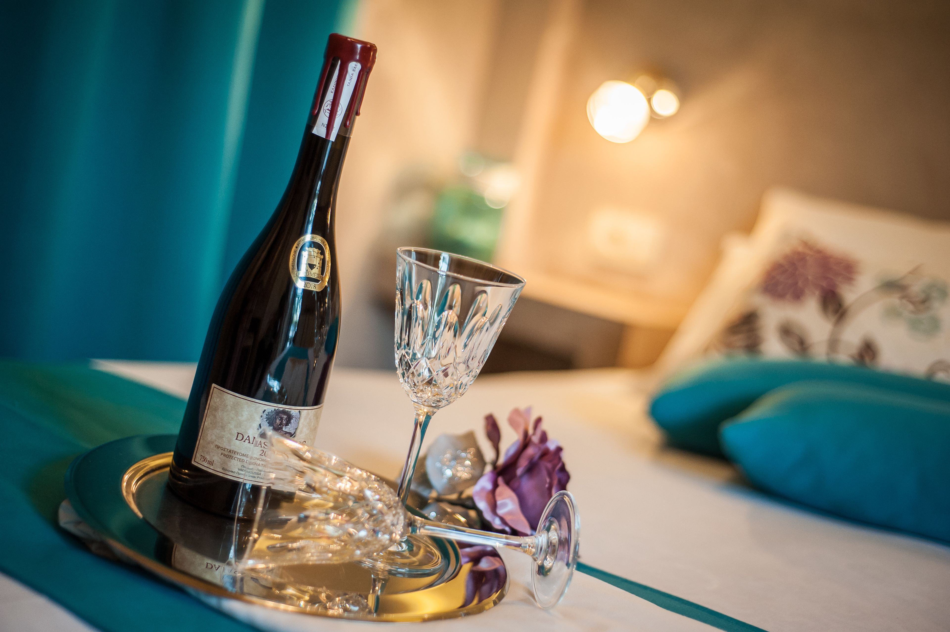 A bottle of wine and a glass on a tray in a room with a bed and pillows.