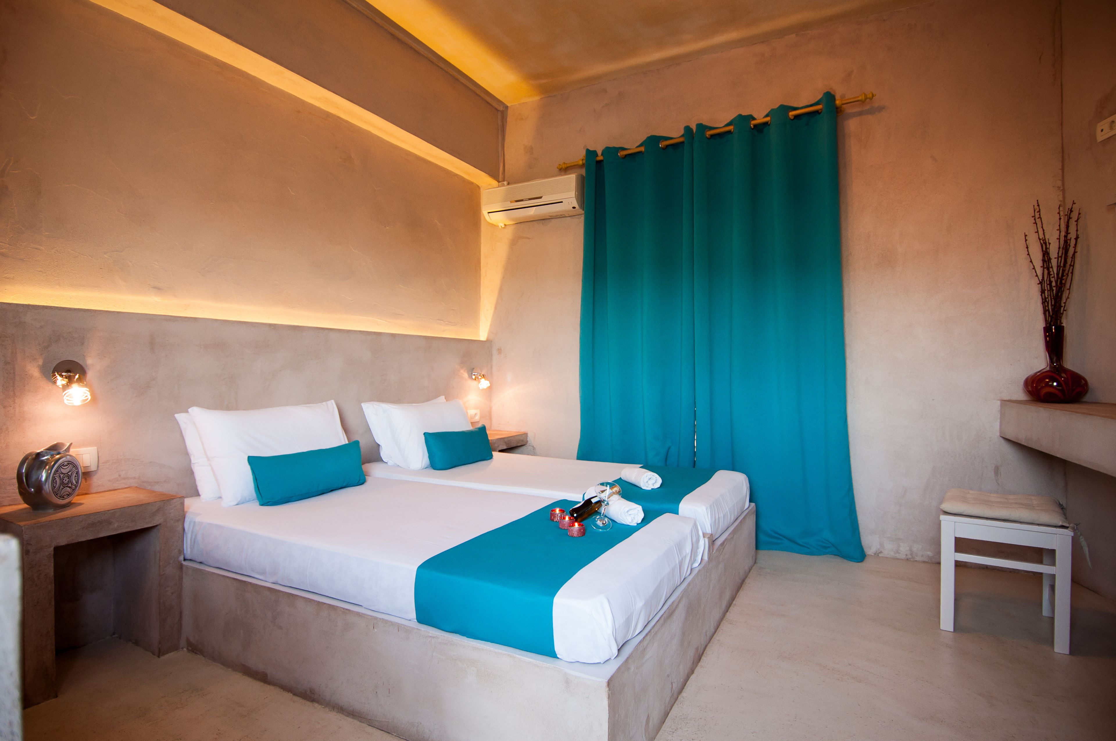 A bedroom with a bed, bedside tables, a nightstand, a small stool, and a wall-mounted air conditioning unit.