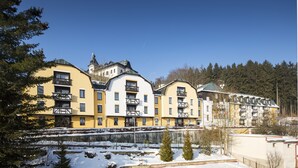 Una hilera de edificios de varios pisos con balcones, suelo cubierto de nieve y un fondo boscoso.