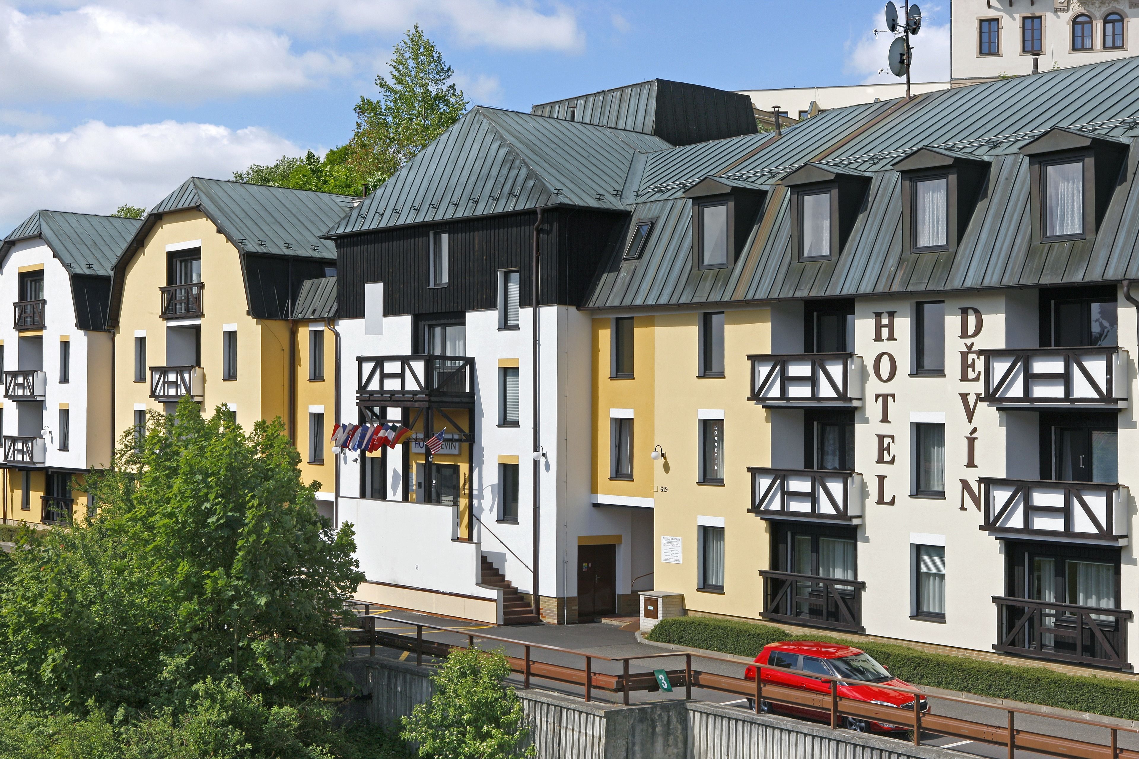 A hotel with multiple balconies, a flag, and a red car parked in front.
