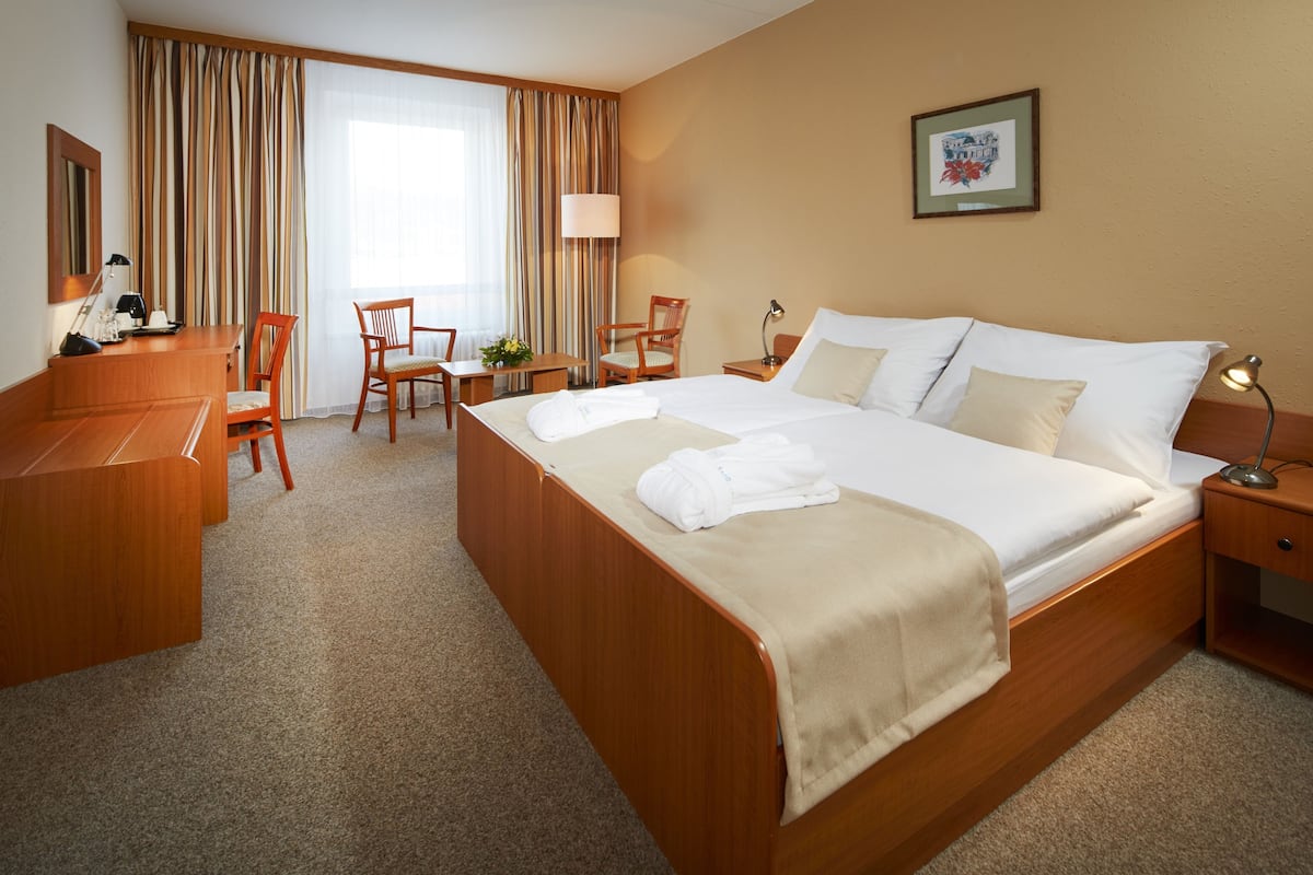 Una camera d'albergo con un letto grande, una scrivania, due poltrone, una lampada e un quadro appeso al muro.