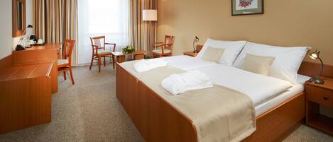 A hotel room with a large bed, a desk, two chairs, a lamp, and a framed picture on the wall.