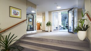 Un vestíbulo de hotel con una escalera alfombrada, un mostrador de recepción y plantas en macetas.