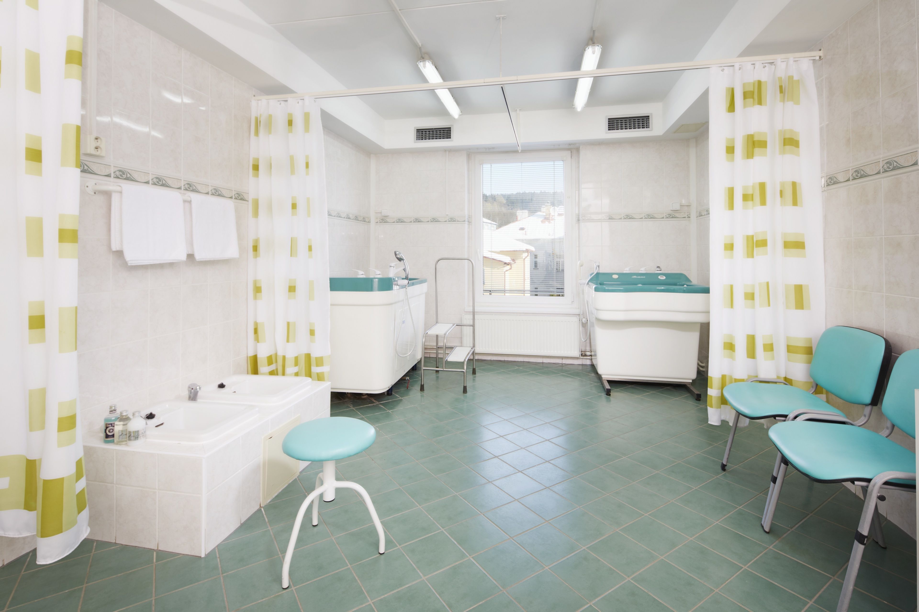 Un baño con dos lavamanos, una bañera y una cortina de ducha. Hay dos sillas y un taburete.