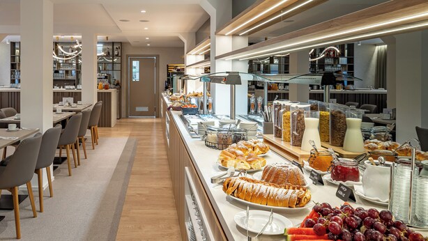 Un moderno bufé de desayuno con diversas opciones de comida y una zona de estar con mesas y sillas.