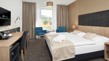 Habitación de hotel con cama, escritorio, sillas, televisión y ventana con vistas.