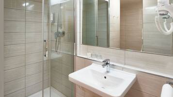 A modern bathroom with a glass shower enclosure, a white sink, and a large mirror.