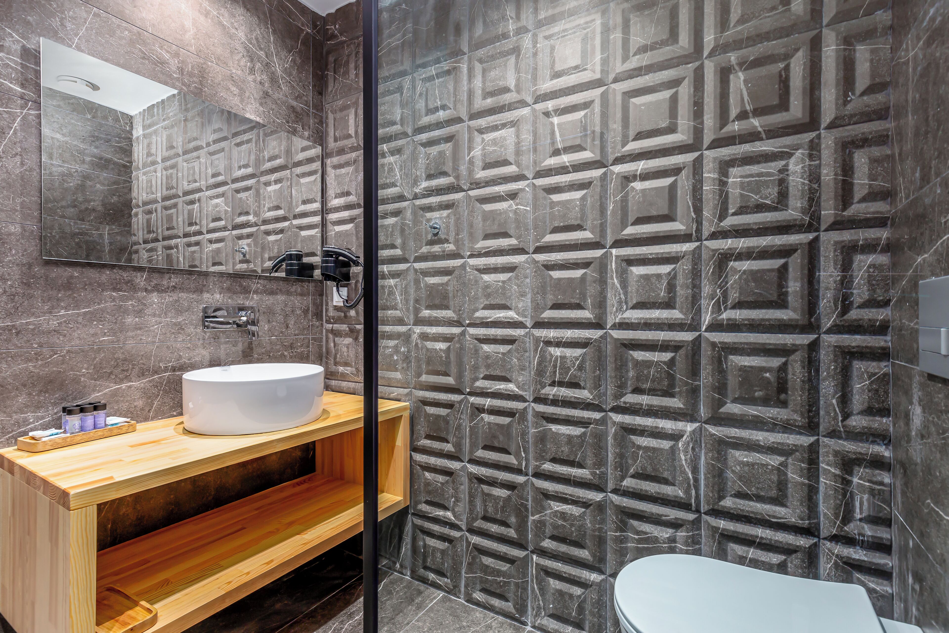 Un baño moderno con un espejo grande, un tocador de madera, un lavabo blanco y una pared con un estampado geométrico.