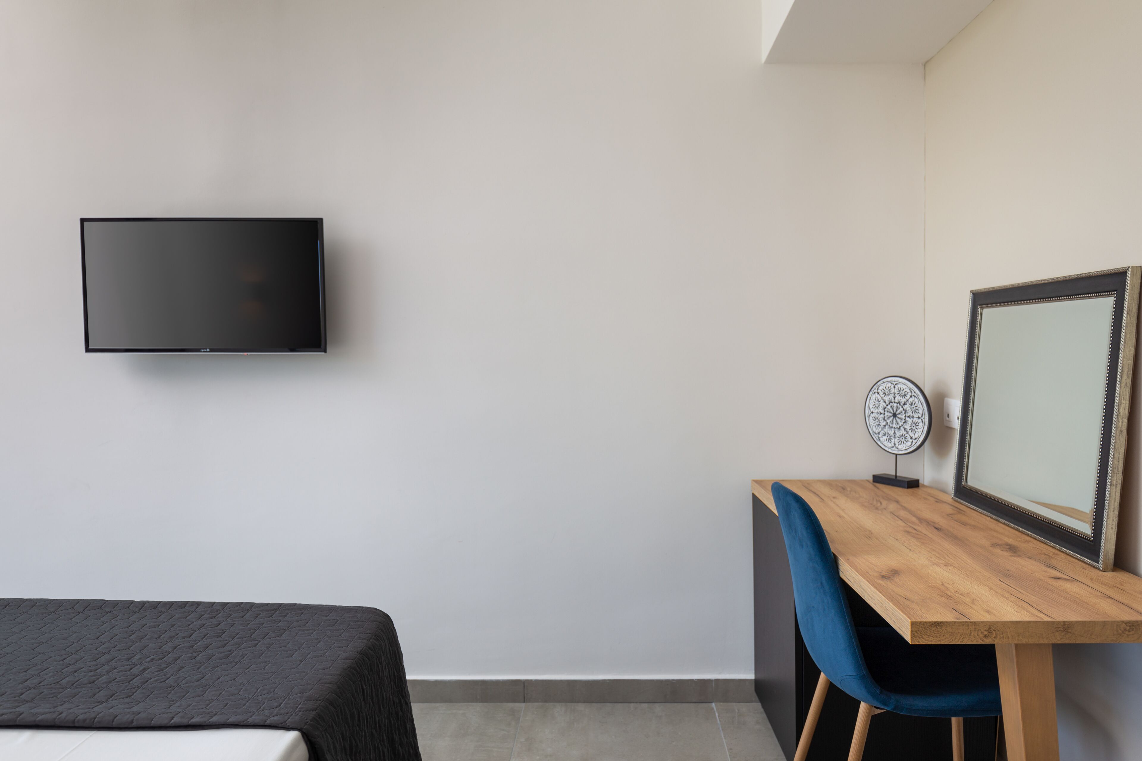 Une chambre moderne comprenant un lit, un bureau avec une chaise, un téléviseur fixé au mur et un miroir décoratif.