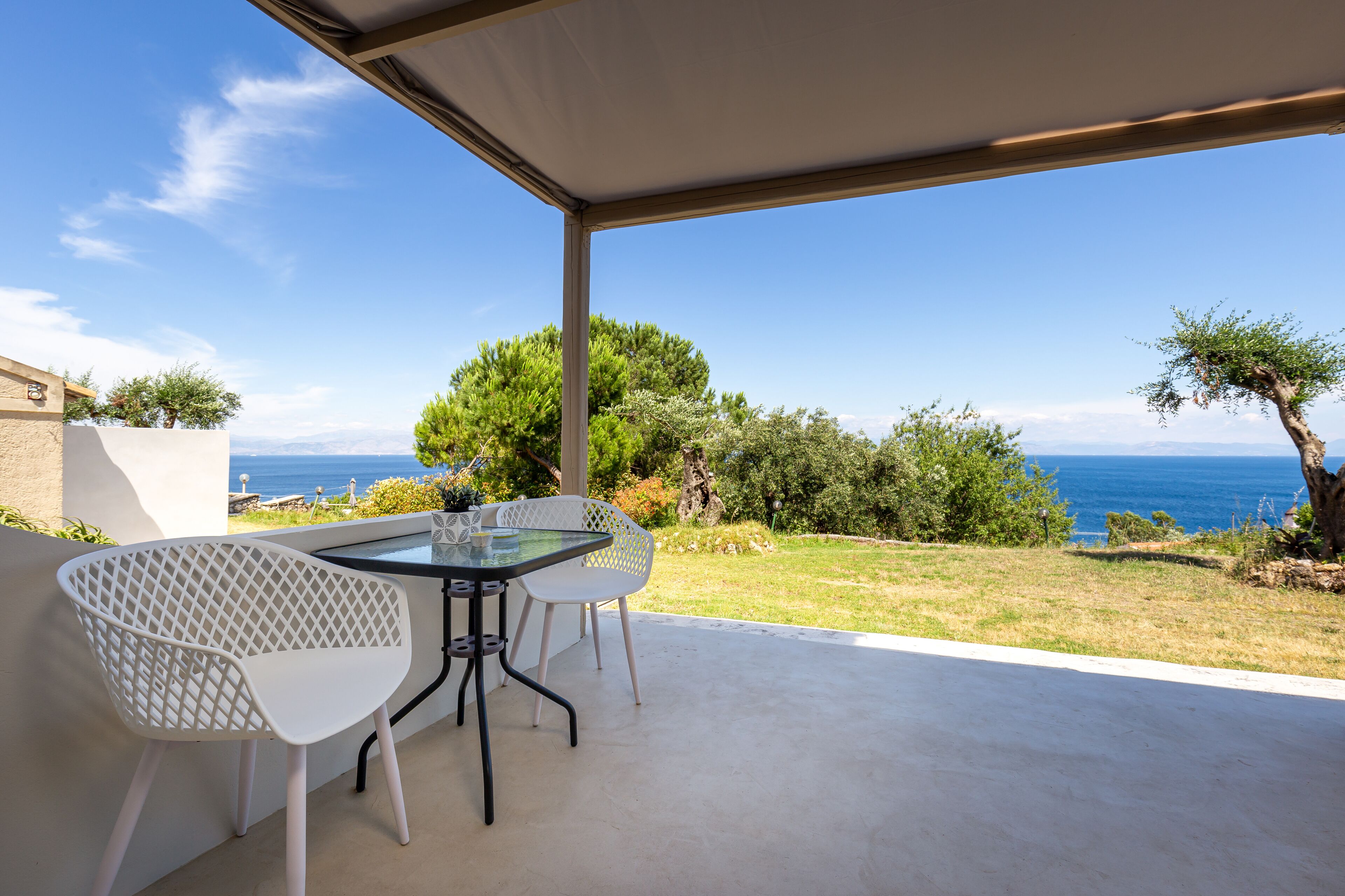 An outdoor patio with a table and chairs, overlooking a scenic view of the sea and greenery.