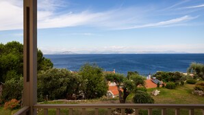 A coastal view from a covered balcony overlooking a sea with distant mountains, surrounded by greenery and a small building with a red roof. - Anasa Corfu (Corfu)