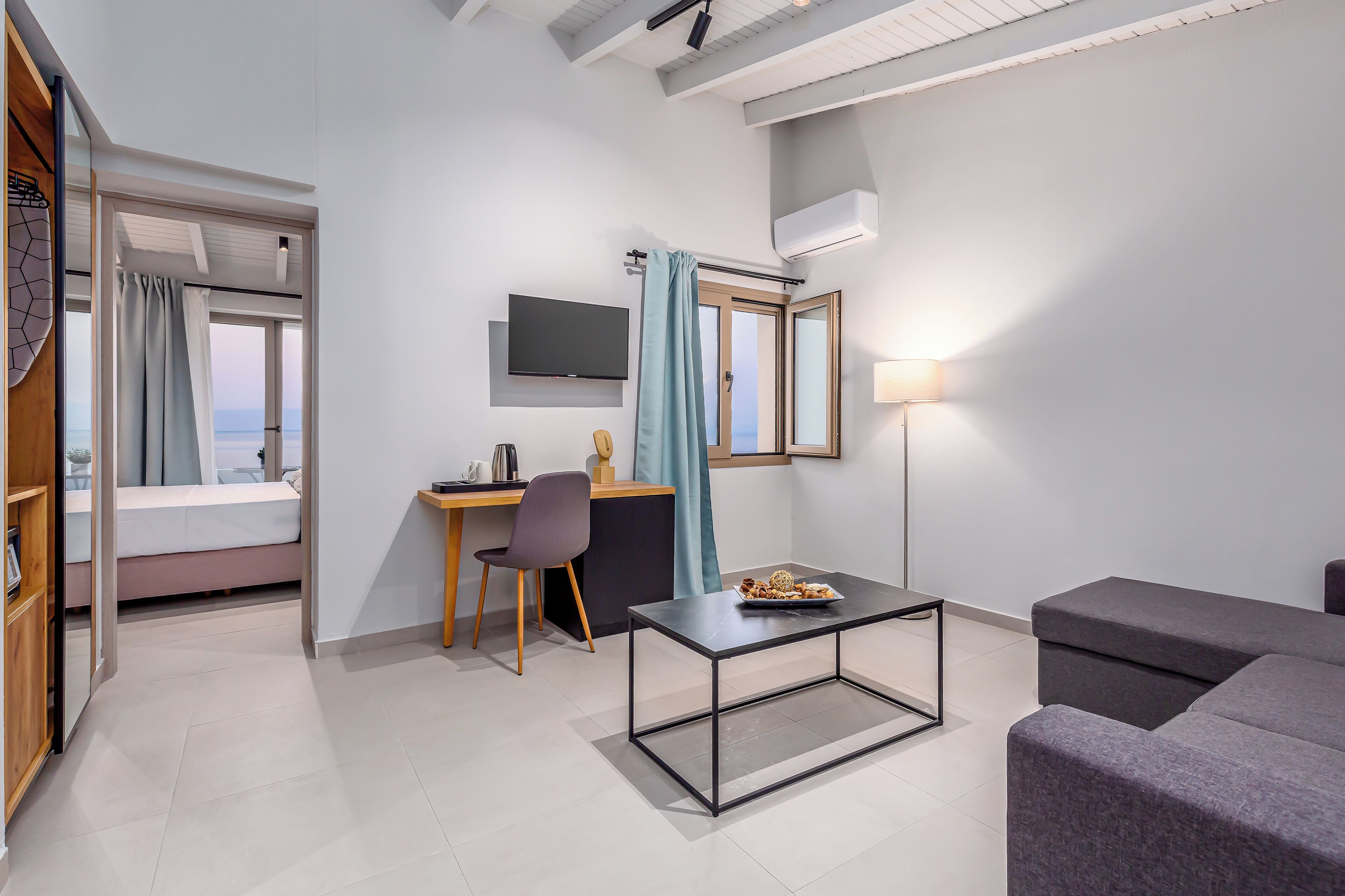 A modern hotel room with a bed, a desk, a television, a lamp, and a sofa.