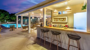 An outdoor bar area with a pool, bar stools, and a stone wall backdrop. - Anasa Corfu (Corfu)