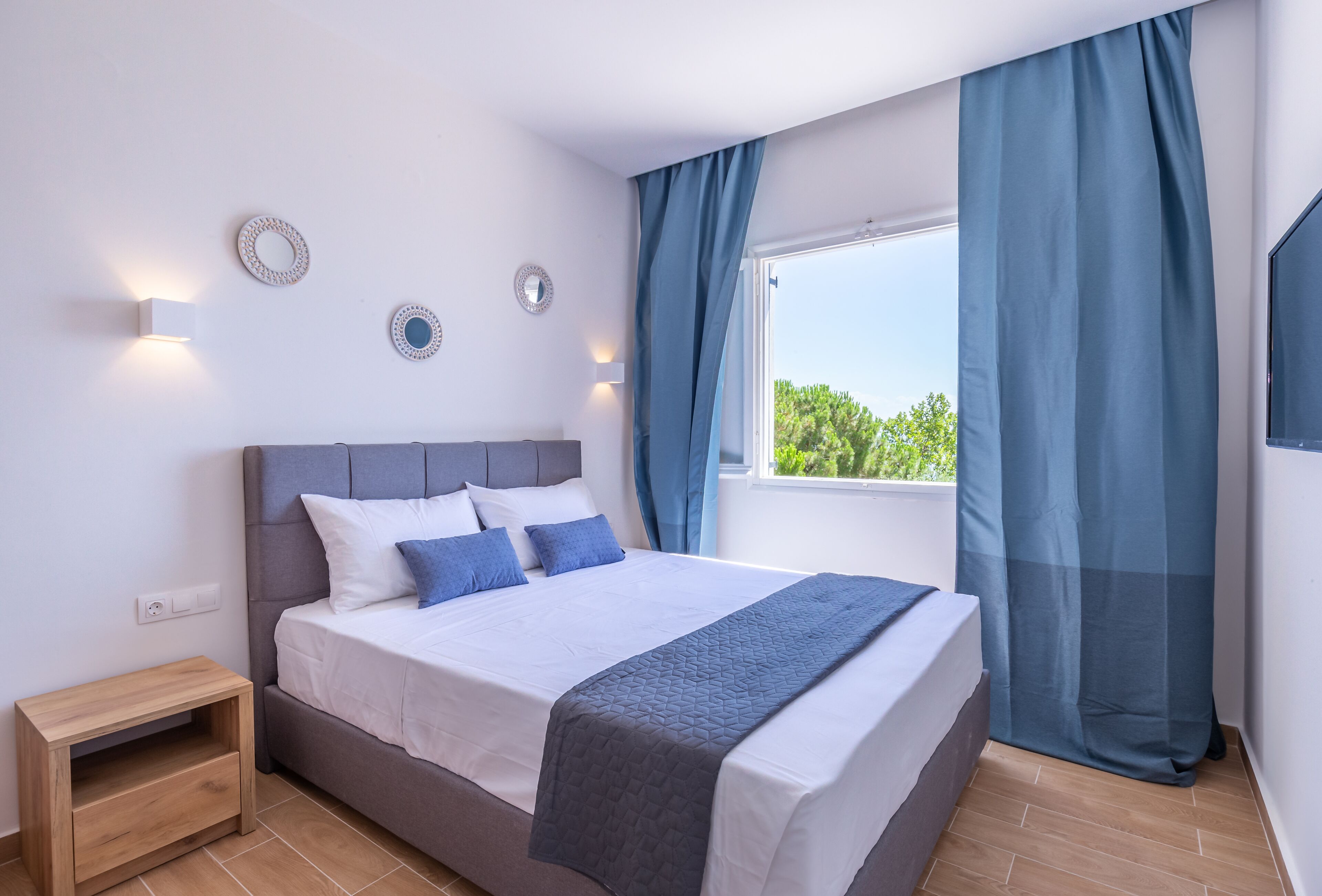 Un dormitorio moderno con una cama grande, una mesita de noche, una ventana con cortinas e iluminación en la pared.