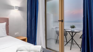 A hotel room with a bed, a nightstand, a small table with a plant, and a view of the sea through a glass door. - Anasa Corfu (Corfu)