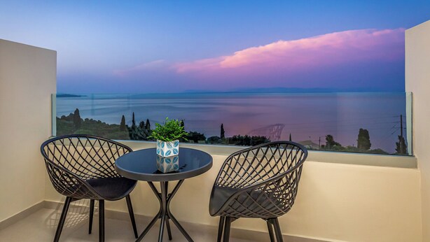 A balcony with two chairs and a table, overlooking a scenic view of a body of water and distant landscape during twilight. - Anasa Corfu (Corfu)