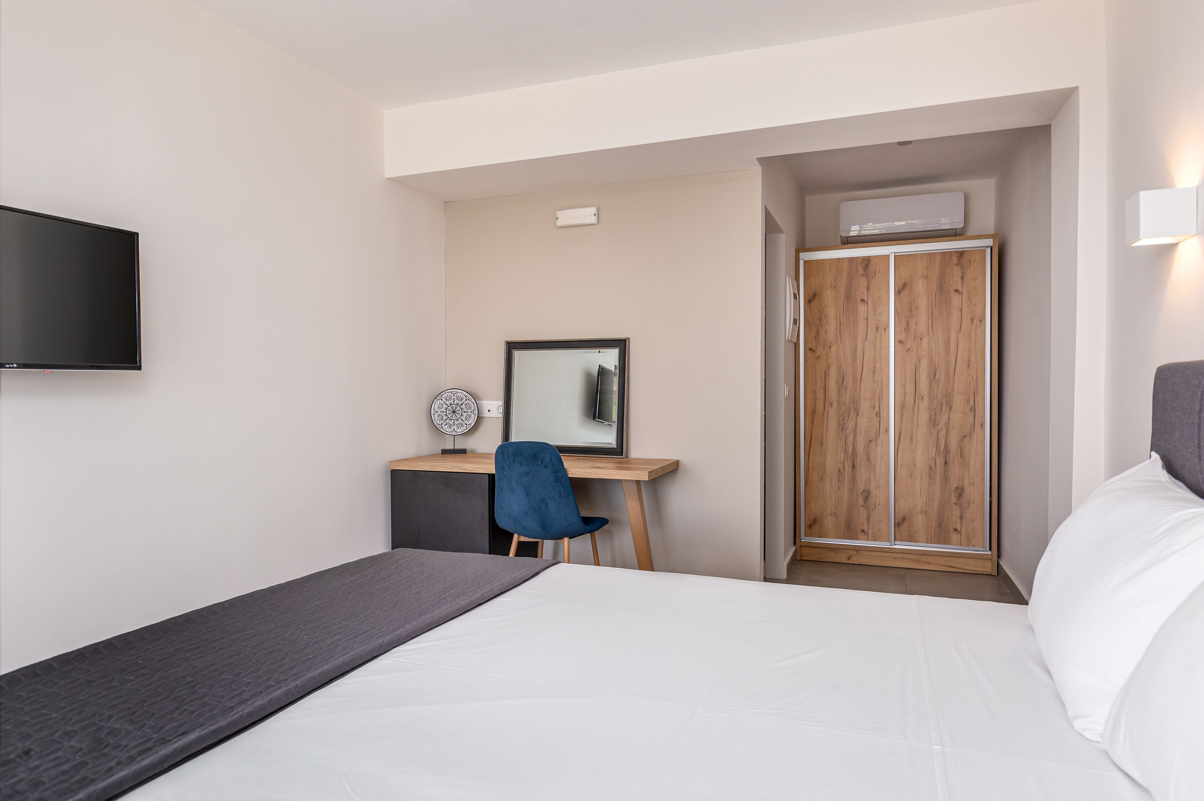 A hotel room with a bed, a desk with a chair, a TV, and a wardrobe.