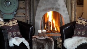 Une pièce chaleureuse avec une cheminée, deux fauteuils en cuir recouverts de plaids en fourrure et une petite table sur laquelle sont posées deux boissons.