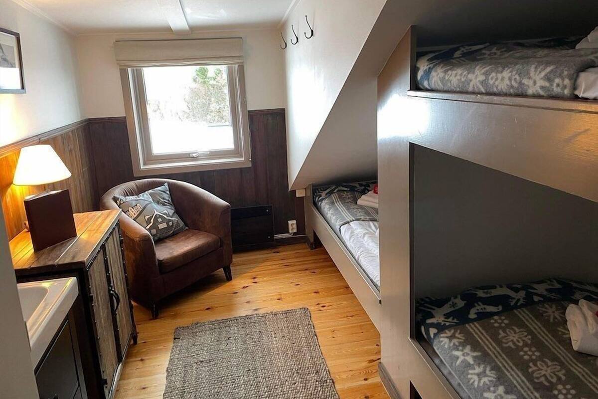 A compact room with a bunk bed, a desk with a lamp, a chair, and a window.