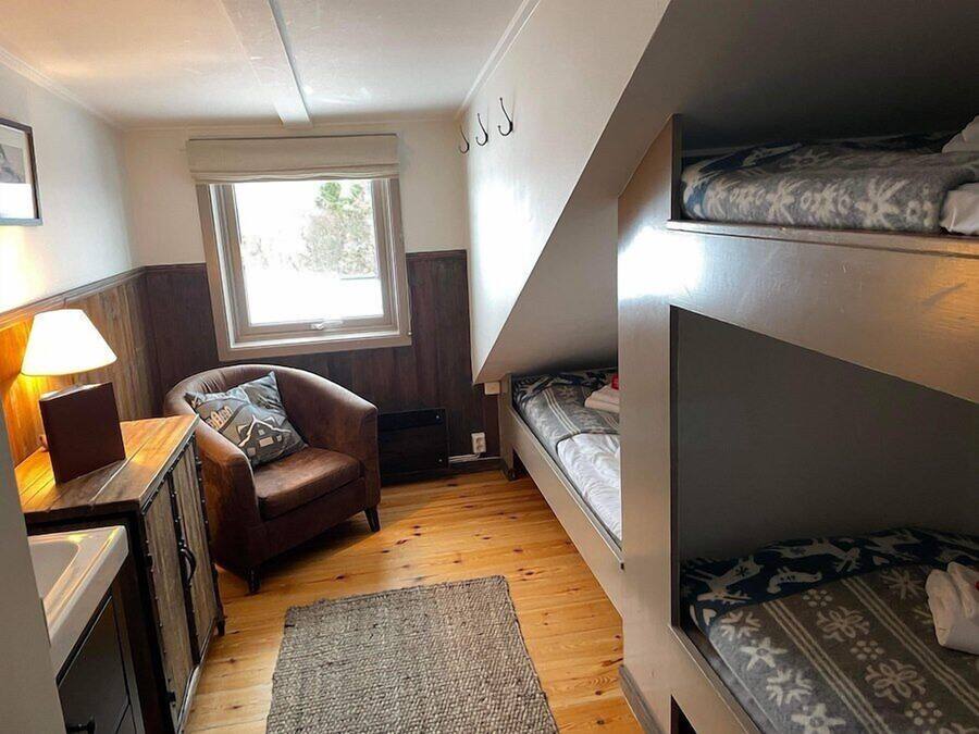 A compact room with a bunk bed, a desk with a lamp, a chair, and a window.