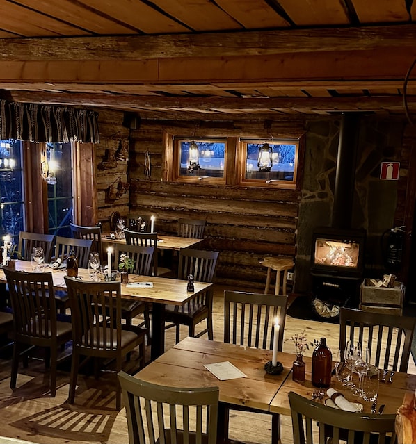 A rustic wooden cabin interior with a dining area, wooden tables, chairs, and a fireplace. - Buustamons Fjällgård (Are)