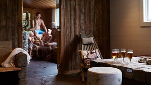 Une pièce rustique en bois, avec un banc, une table sur laquelle sont posés des verres de bière et une porte en bois donnant sur une autre pièce.