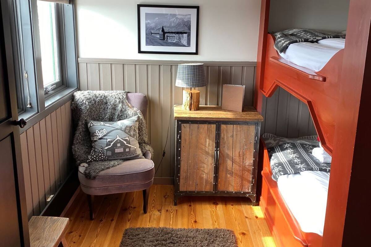 A compact room with a bunk bed, a cushioned chair, a small cabinet, and a framed picture on the wall.