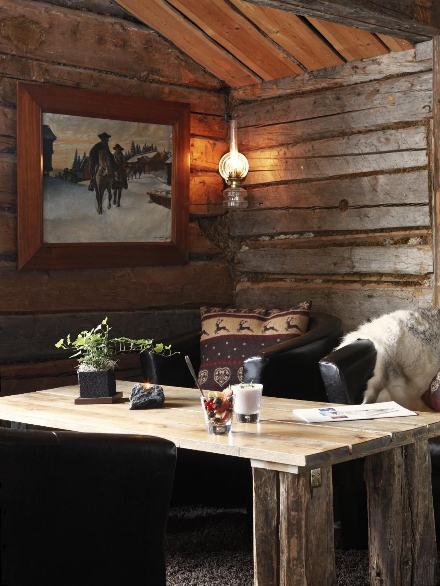 Interior rústico de una cabaña con una mesa de madera, un cuadro enmarcado, una lámpara y un sofá.