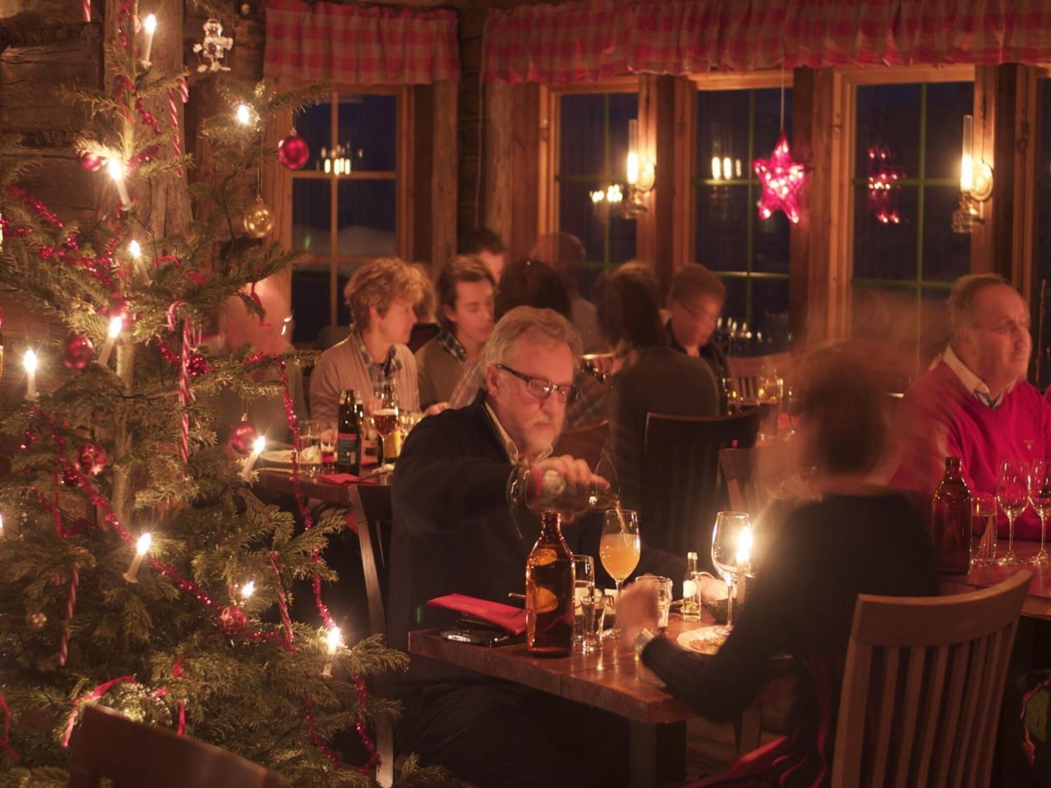 Un ristorante accogliente con un albero di Natale, tavoli in legno e persone che cenano.