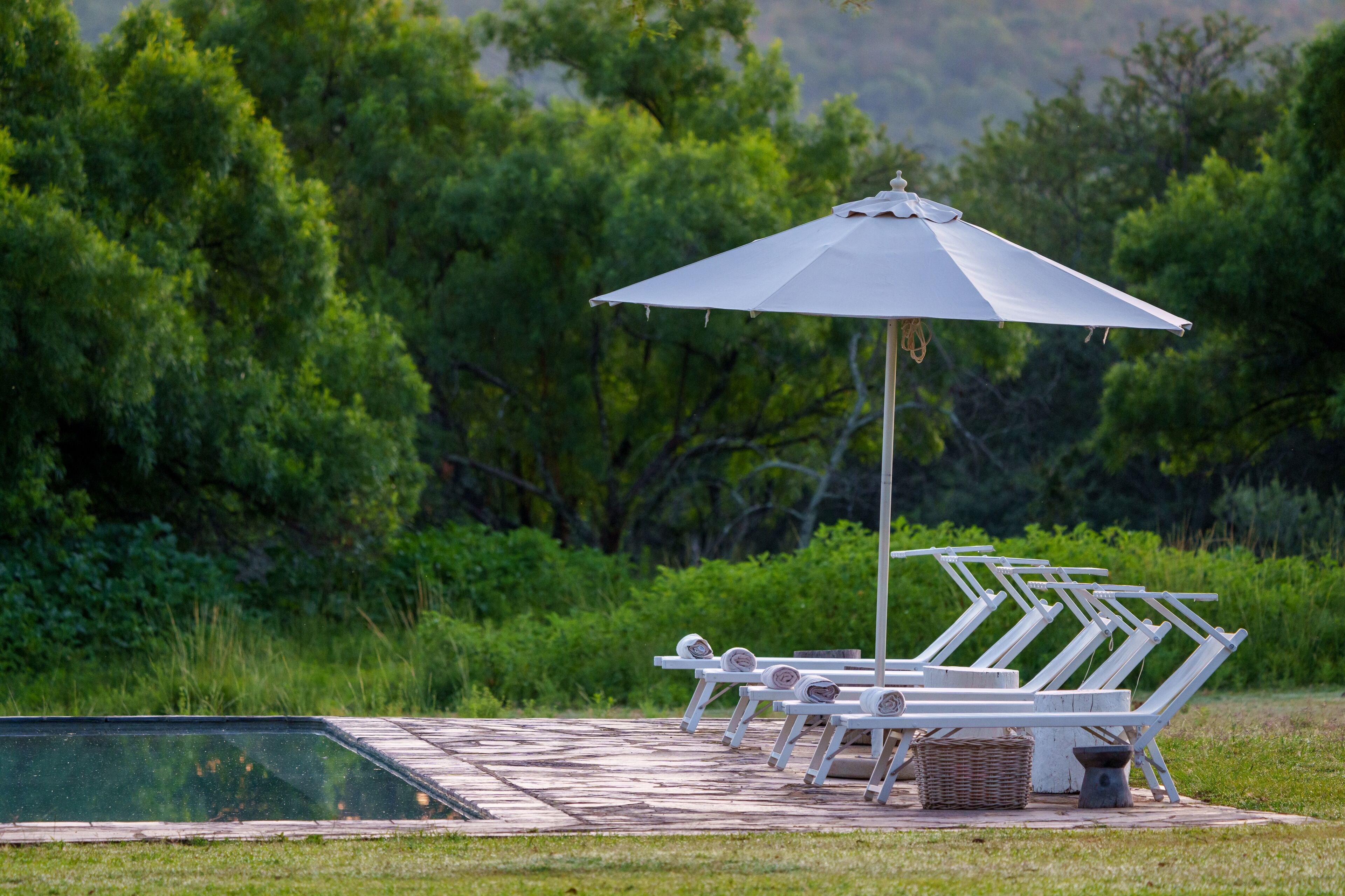 A poolside area with white lounge chairs and a large umbrella.
