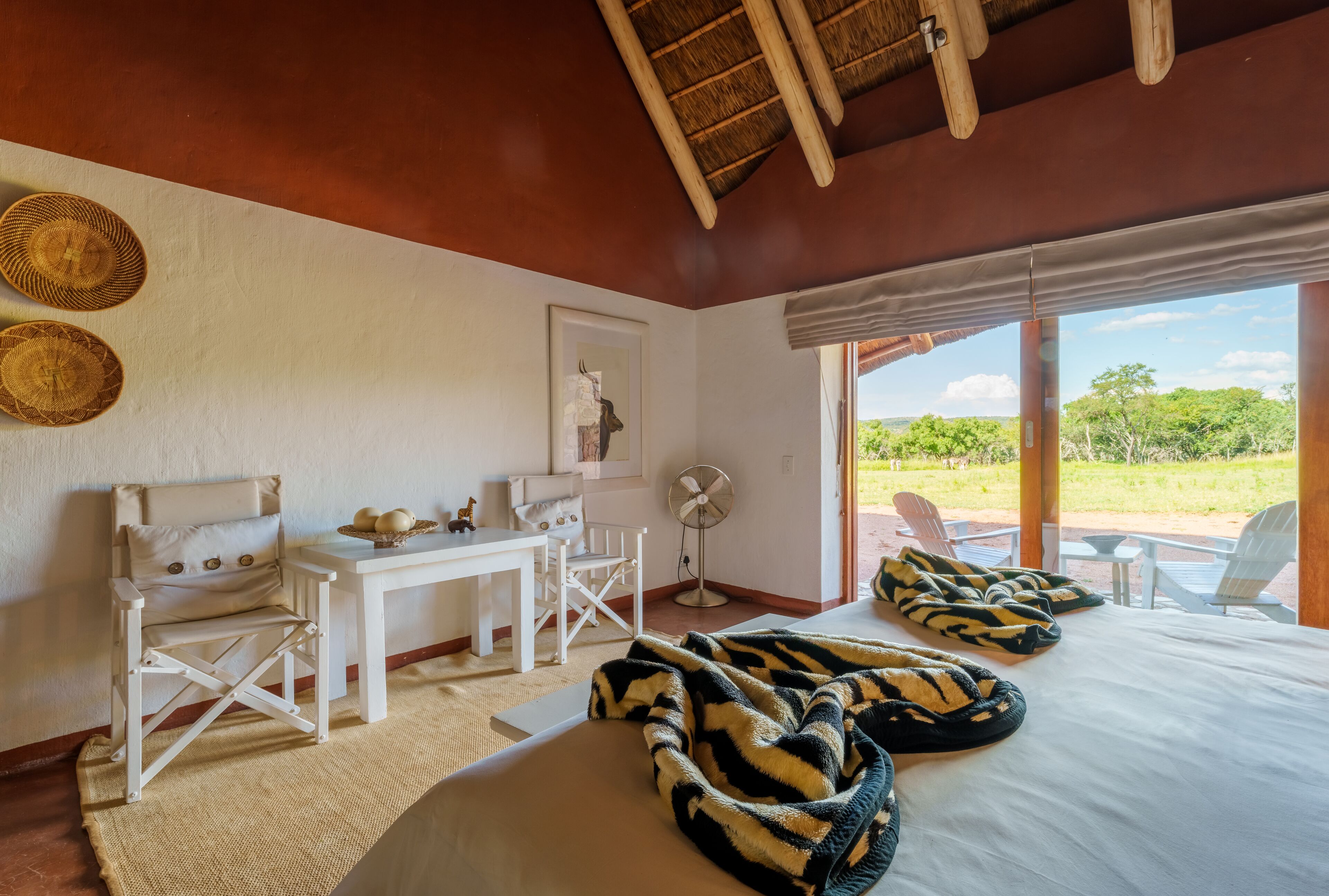 A room with a bed, a table, chairs, a fan, and a view of the outdoors.