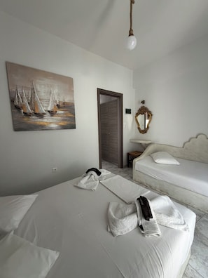A hotel room with a bed, a sofa, a painting of sailboats, a mirror, and a hanging light fixture. - Foinikas Studios (Kithnos)