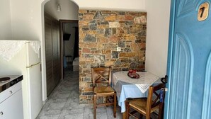 A compact kitchen with a dining area, a stone wall, and a blue door with the number 7. - Foinikas Studios (Kithnos)