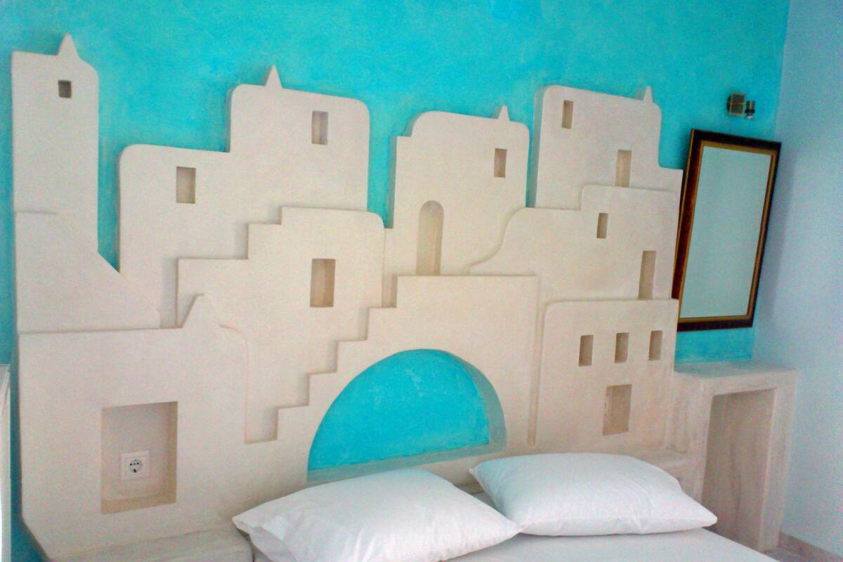 A bed with white bedding and two pillows, a wall with a blue arch, and a white wall-mounted mirror.
