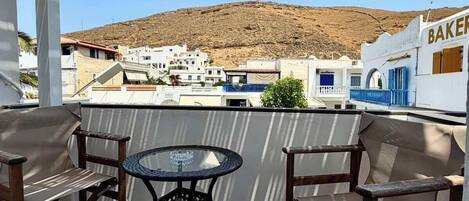 A covered outdoor seating area with a table and chairs, overlooking a hillside with buildings.