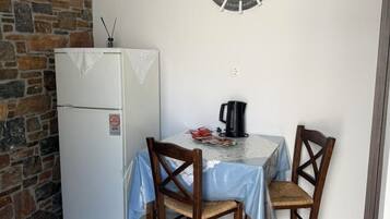 Uma pequena área de refeições com uma mesa, duas cadeiras, um relógio na parede, um frigorífico e uma parede de pedra.